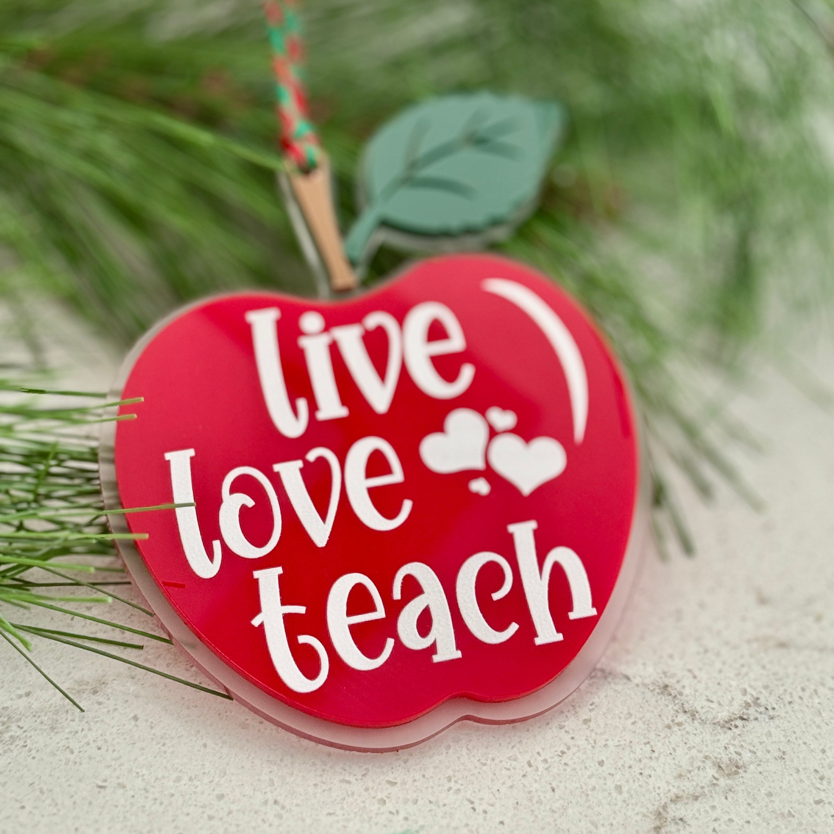 Red apple-shaped ornament with 'Live Love Teach' text on a Christmas tree branch.