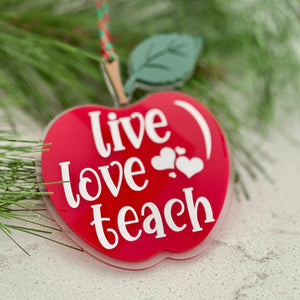 Red apple-shaped ornament with 'Live Love Teach' text on a Christmas tree branch.