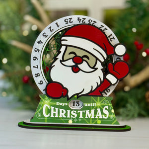 Christmas countdown timer with Santa Claus design on a white surface with a blurred green background.