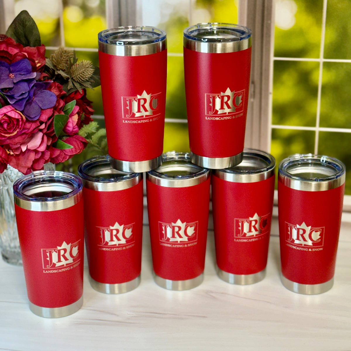 Red tumblers with a logo on a white surface with flowers in the background