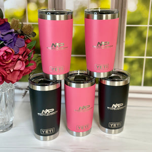 Pink and black YETI tumblers stacked on a surface with flowers in the background