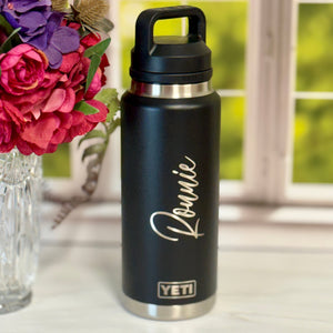 Black YETI water bottle with 'Ronnie' engraving on a white surface with flowers in the background