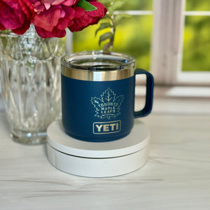 Blue YETI mug with Toronto Maple Leafs logo on a coaster, surrounded by flowers.