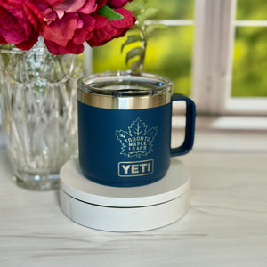 Blue YETI mug with Toronto Maple Leafs logo on a coaster, surrounded by flowers.